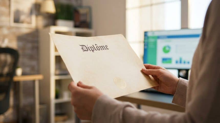 Anonymous hands gently hold a French diploma with a subtle seal. Blurred modern office background with a digital screen suggests new opportunities.