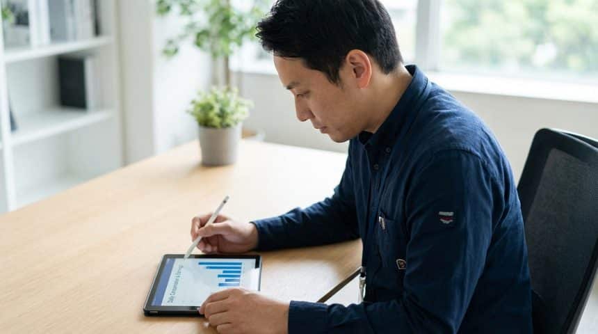 A focused professional in a dark blue shirt reviews daily compensation on a tablet with a stylus in a modern office.