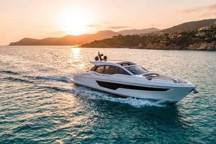 White luxury yacht with dark windows on vibrant turquoise water at golden hour, with a sun-drenched coastline and villas.