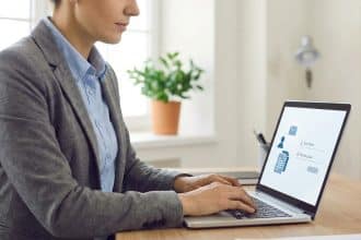 Professional in grey blazer typing on laptop displaying a login screen with 'Identifiant' and 'Mot de passe' in a bright, modern office.
