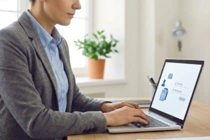 Professional in grey blazer typing on laptop displaying a login screen with 'Identifiant' and 'Mot de passe' in a bright, modern office.