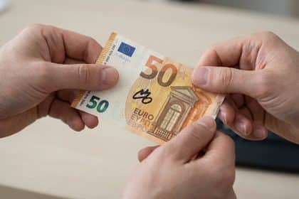 Close-up of two hands holding a 50 Euro banknote with a prominent black felt-tip pen mark against a blurred light background.