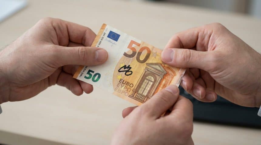 Close-up of two hands holding a 50 Euro banknote with a prominent black felt-tip pen mark against a blurred light background.