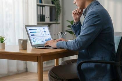 A person, representing a teacher, focused on a laptop displaying abstract career management data in a modern, naturally lit home office.