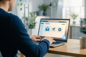 Homme tapant sur un ordinateur portable. L'écran affiche une interface webmail avec des icônes d'enveloppe, d'envoi et un cadenas de sécurité.