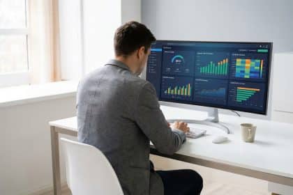 Un homme en veste grise, vu de dos, utilise un ordinateur pour analyser un tableau de bord SEO détaillé avec graphiques et données.