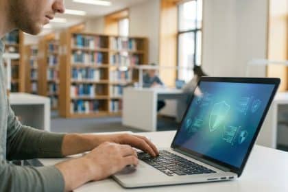 Jeune étudiant tapant sur un ordinateur portable dans une bibliothèque. L'écran affiche un symbole de bouclier pour la sécurité.