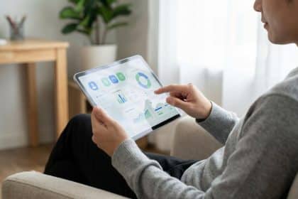 Personne utilisant une tablette affichant un tableau de bord financier avec graphiques, icônes bancaires. Contexte de gestion de compte en ligne.