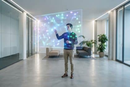 Un homme interagit avec un grand écran holographique lumineux affichant des données dans un bureau moderne.