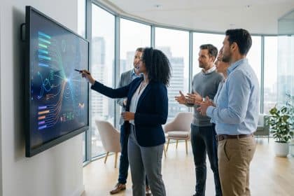 Une femme présente des données sur un écran interactif à quatre collègues attentifs dans un bureau moderne avec vue sur la ville.
