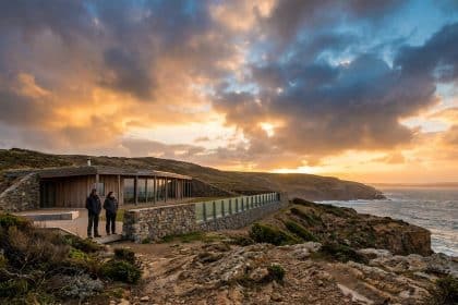 Deux personnes contemplent une maison éco-conçue intégrée dans la falaise au coucher du soleil.